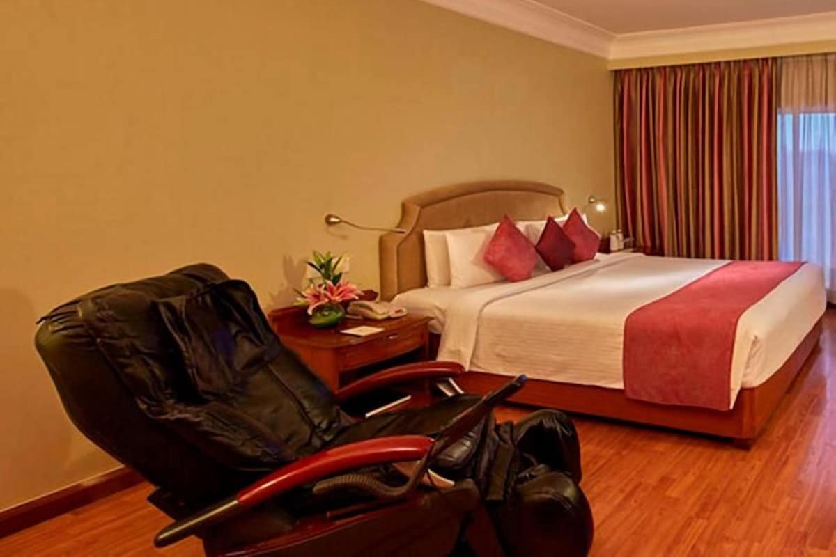 A hotel room with a bed, a chair, a nightstand, and a window with curtains.