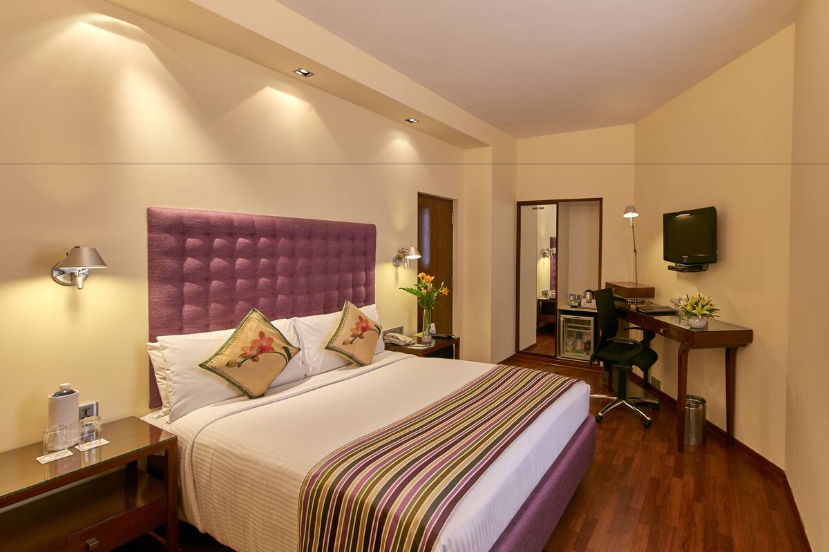 Une chambre d’hôtel avec un grand lit, un bureau, une chaise, une télévision et une salle de bain visible à travers une porte ouverte.