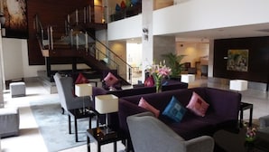 Een ruime lobby met een modern design, met een paarse bank, een trap en een groot schilderij aan de wand.