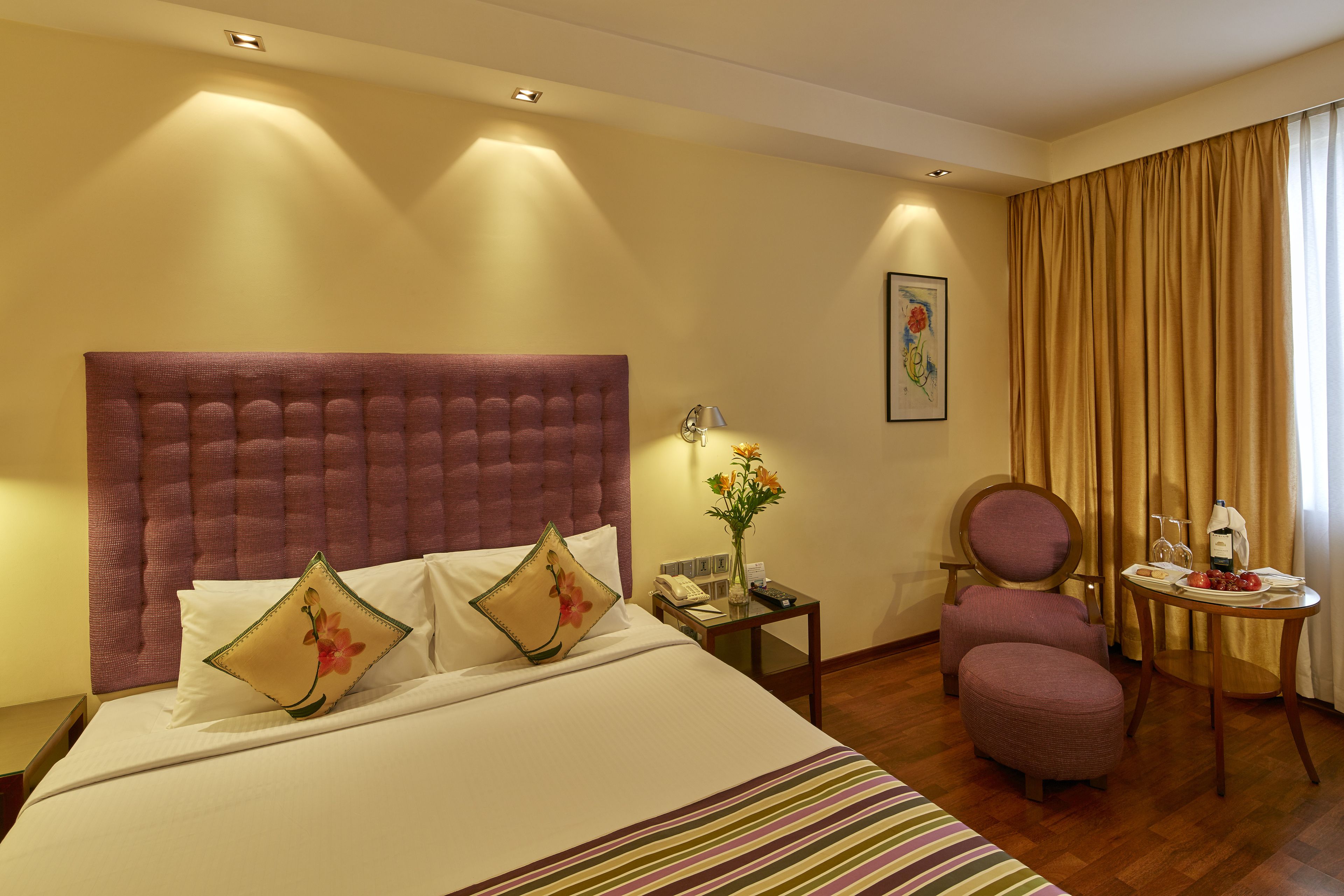 Een hotelkamer met een groot bed, een stoel, een klein tafeltje met een fles en een vaas met bloemen.