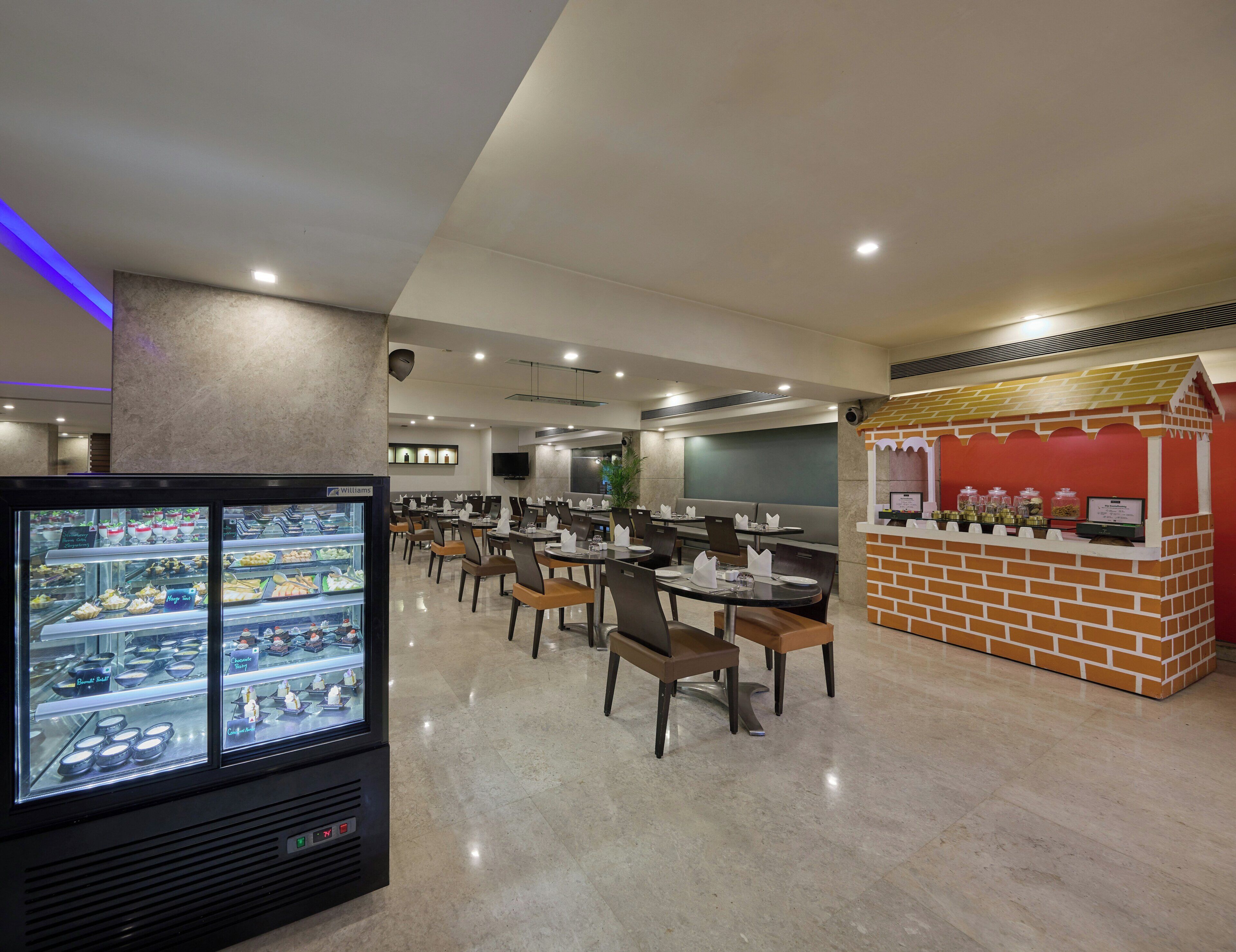 A modern dining area with tables, chairs, a dessert display, and a small kiosk.
