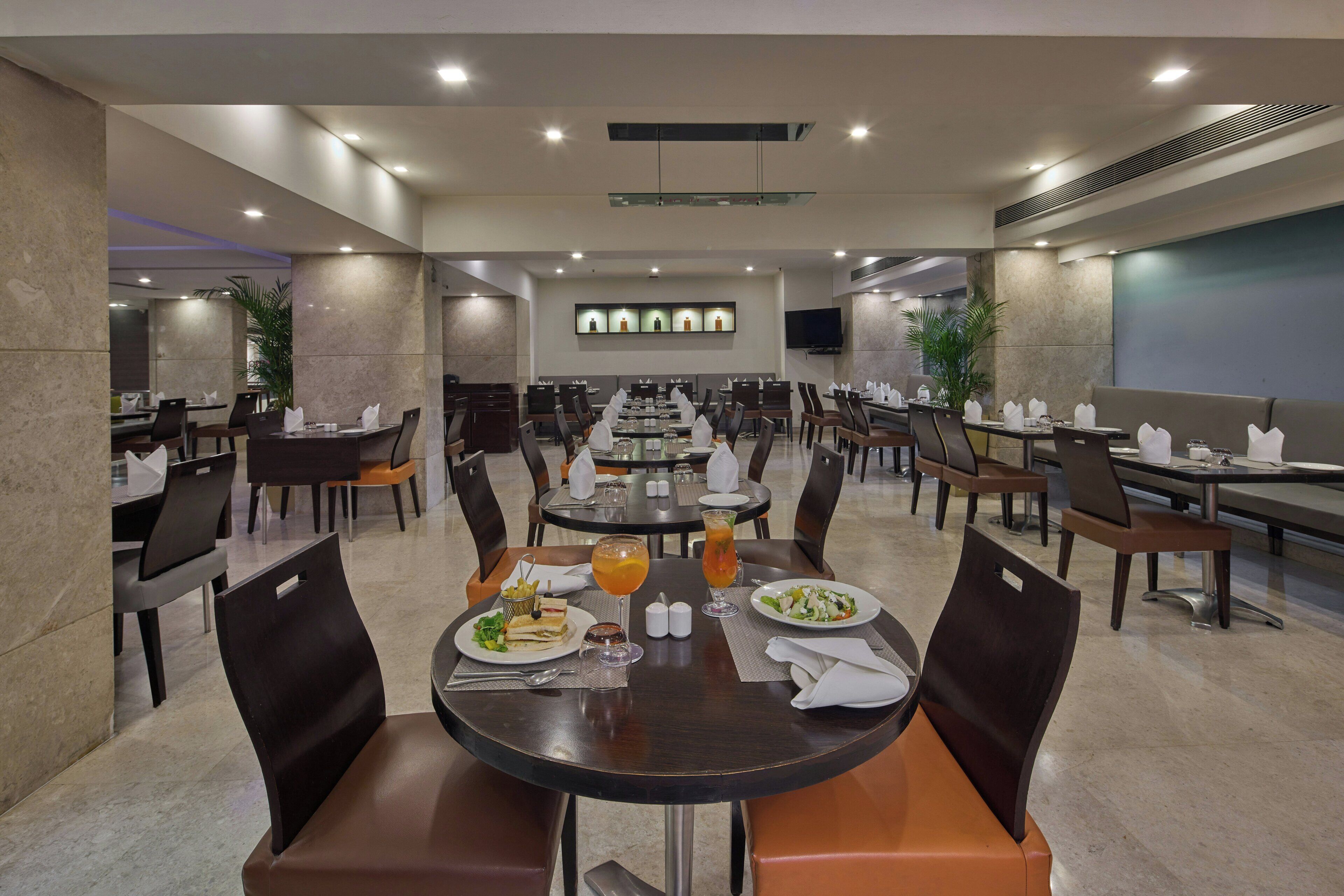A spacious dining area with multiple tables and chairs, a flat-screen TV mounted on the wall, and a modern ceiling design.
