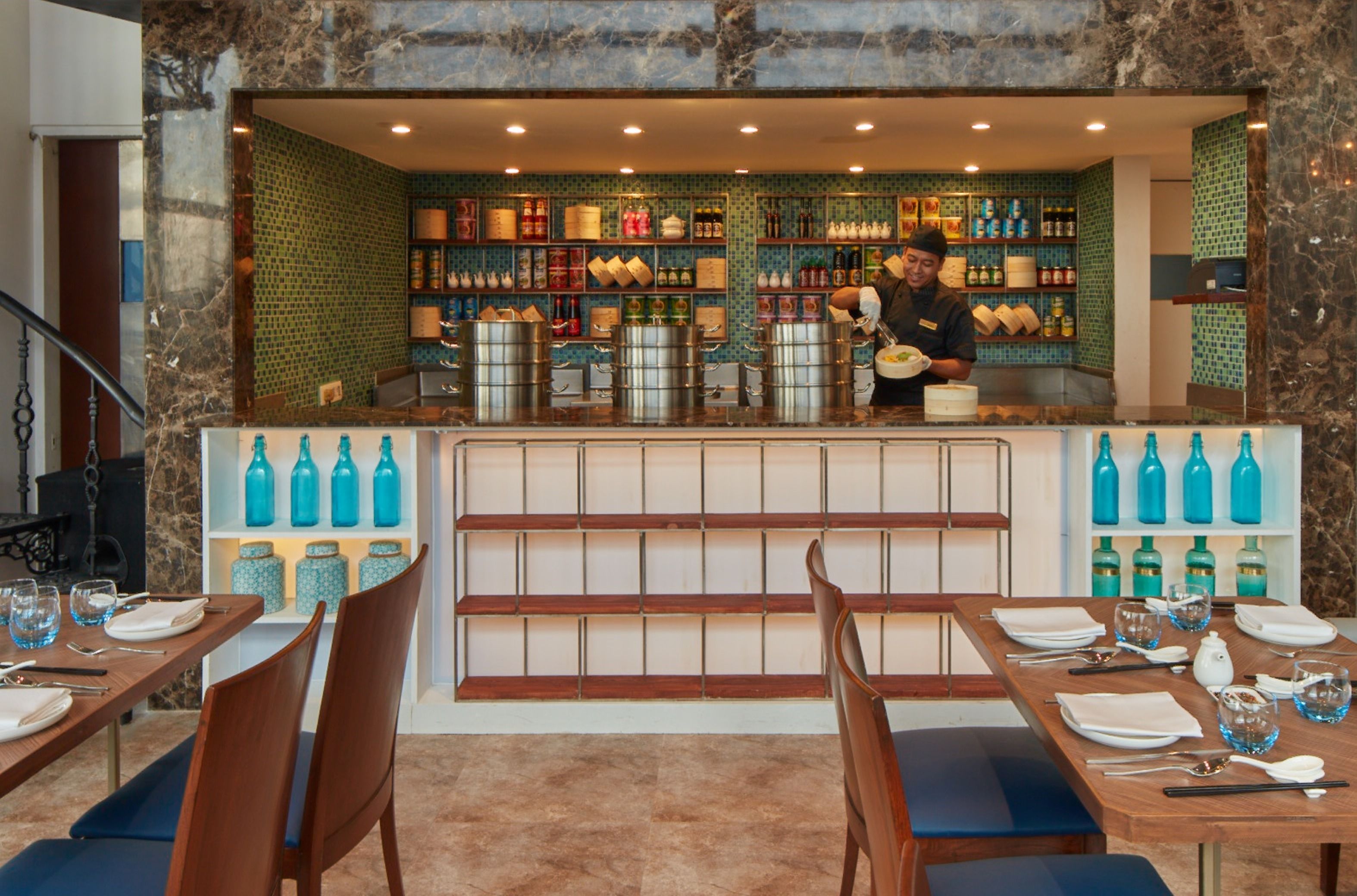 Un restaurant avec un comptoir en marbre, des chaises bleues et une variété de bouteilles et de pots exposés sur des étagères.
