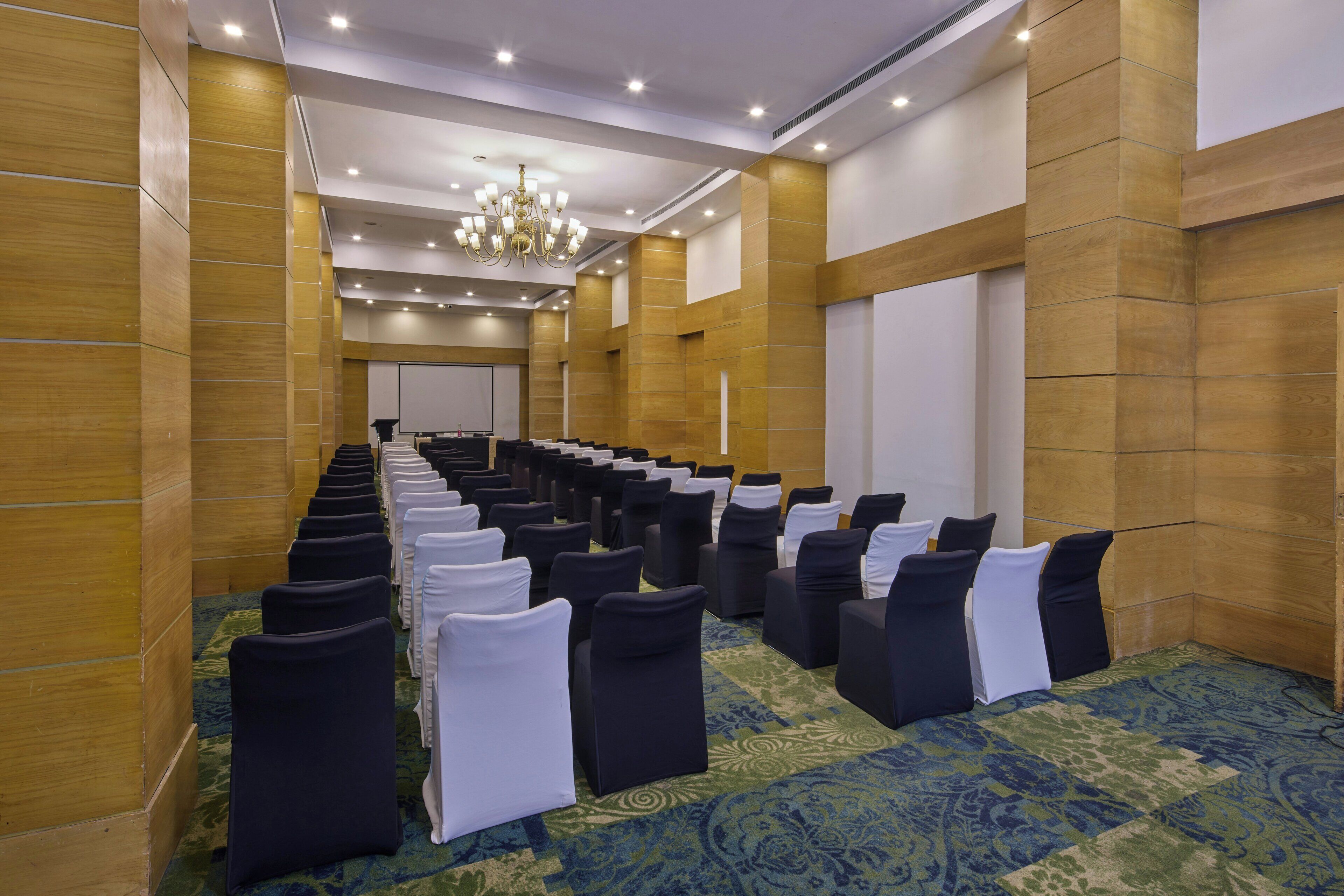 A conference room with rows of chairs, a chandelier, and a large screen at the front.