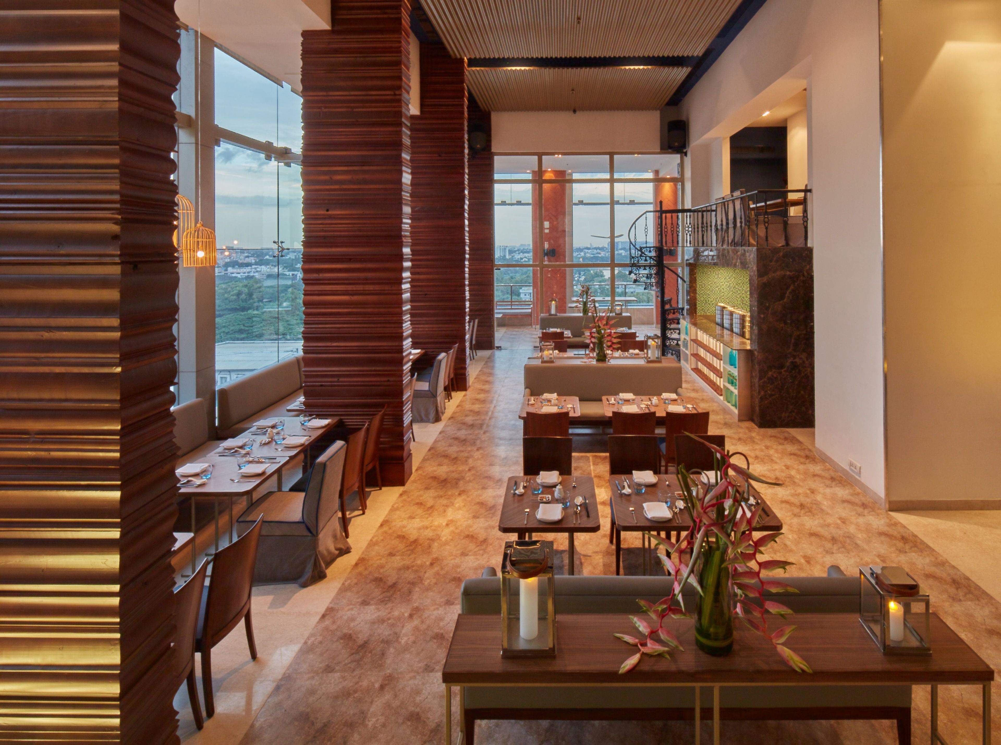 En modern restaurang med en lång matsal, trädetaljer och utsikt över stadsbilden genom stora fönster.