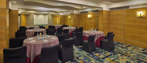A conference room with multiple tables, chairs, and a projector screen.