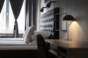 A neatly made bed with white linens, a black headboard, and a bedside table with a lamp. - Hotell Skövde (Skovde)