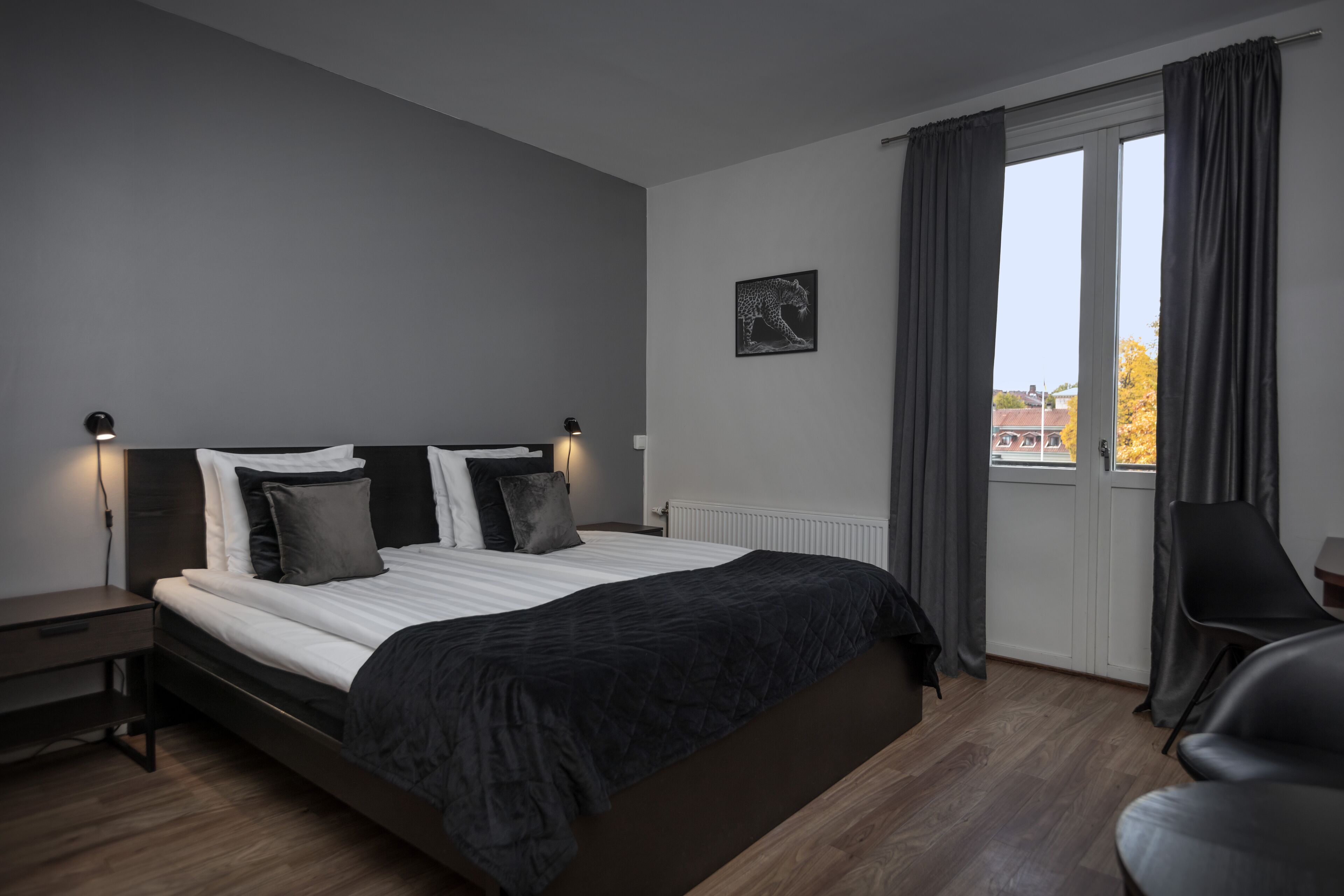 A modern bedroom with a large bed, a nightstand, a chair, and a window with curtains.