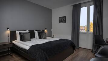 A modern bedroom with a large bed, a nightstand, a chair, and a window with curtains.
