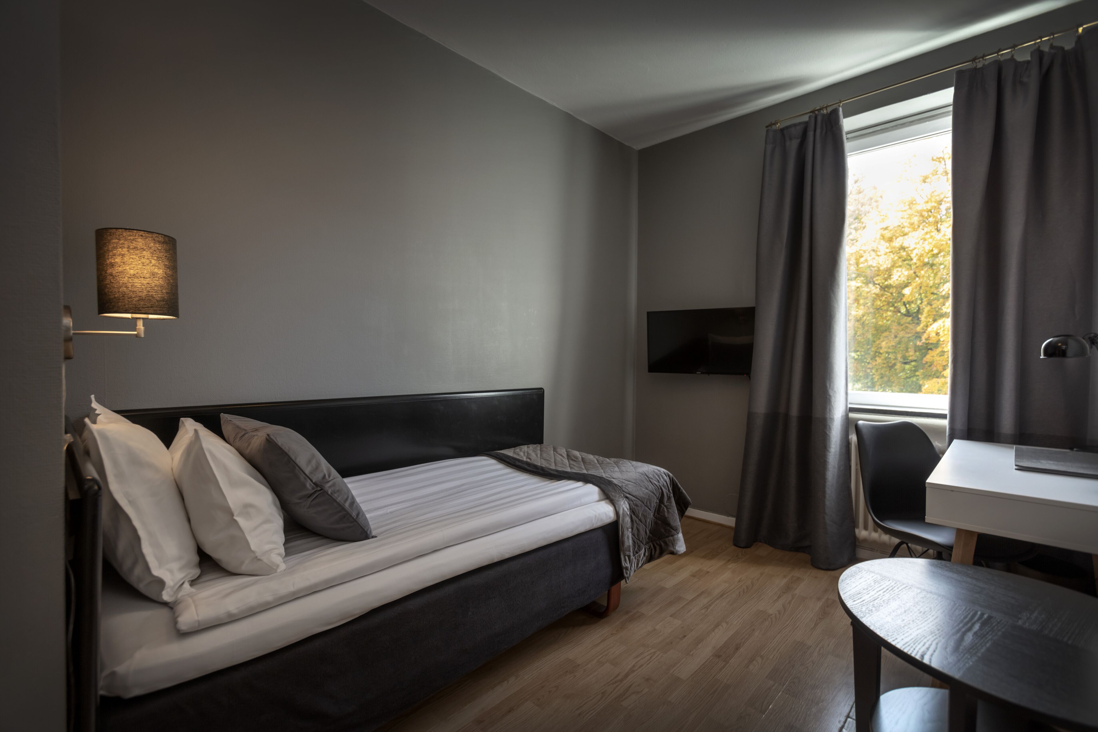 Un dormitorio con cama, escritorio, silla, televisor y ventana con cortinas.