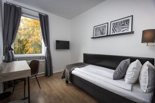 Una habitación de hotel moderna con una cama, un escritorio y una silla. Cuenta con una ventana con cortinas, un televisor de pantalla plana y una obra de arte enmarcada en la pared.