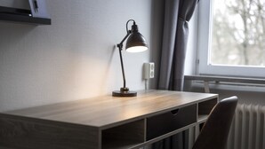 Un escritorio de madera con una lámpara de escritorio negra, una silla y una ventana con cortinas.