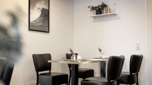 Un área de comedor con una mesa y cuatro sillas, un estante con plantas y un cuadro en la pared.