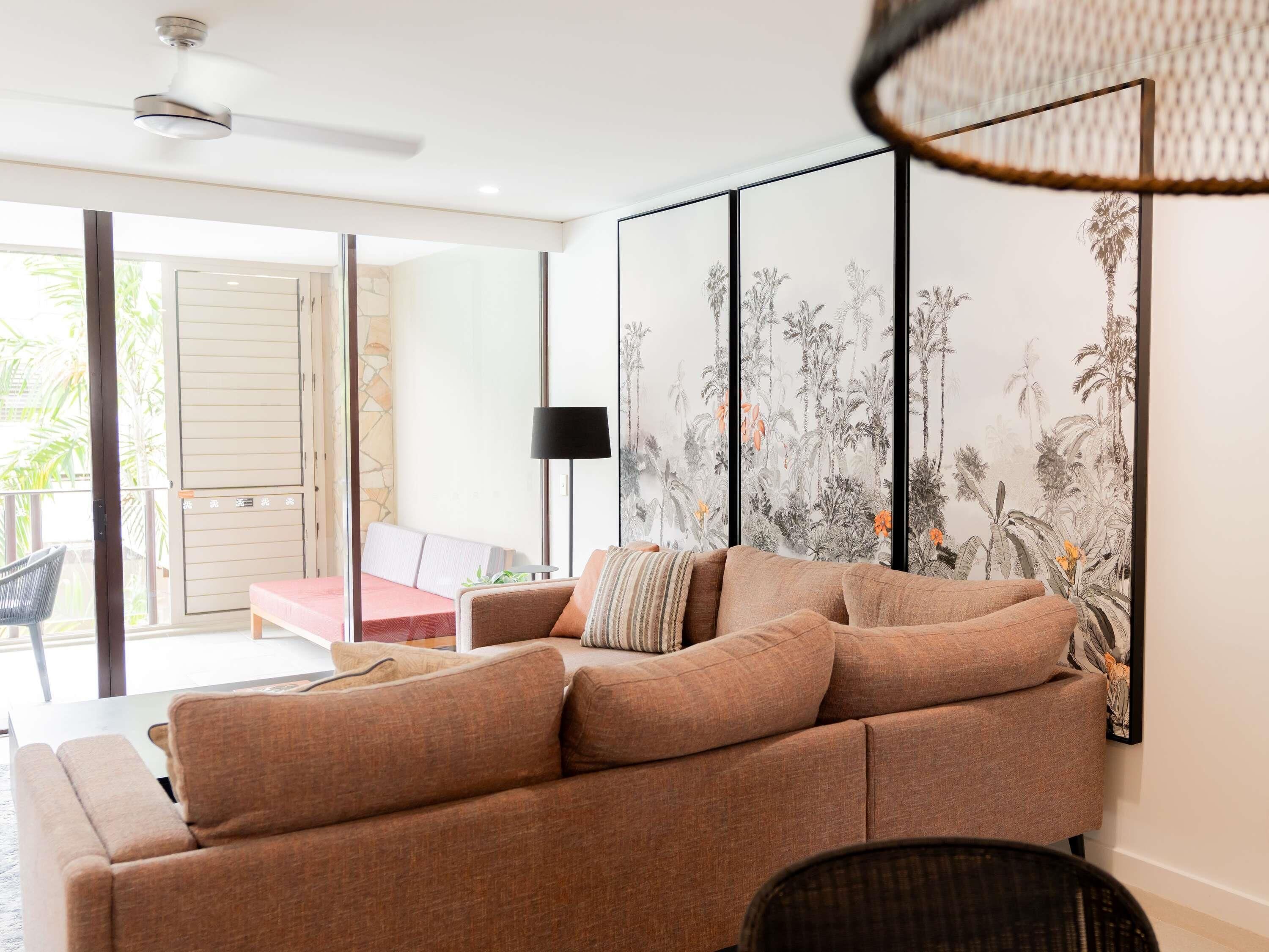 A modern living room with a large sofa, a floor lamp, and a wall with a tropical plant mural.