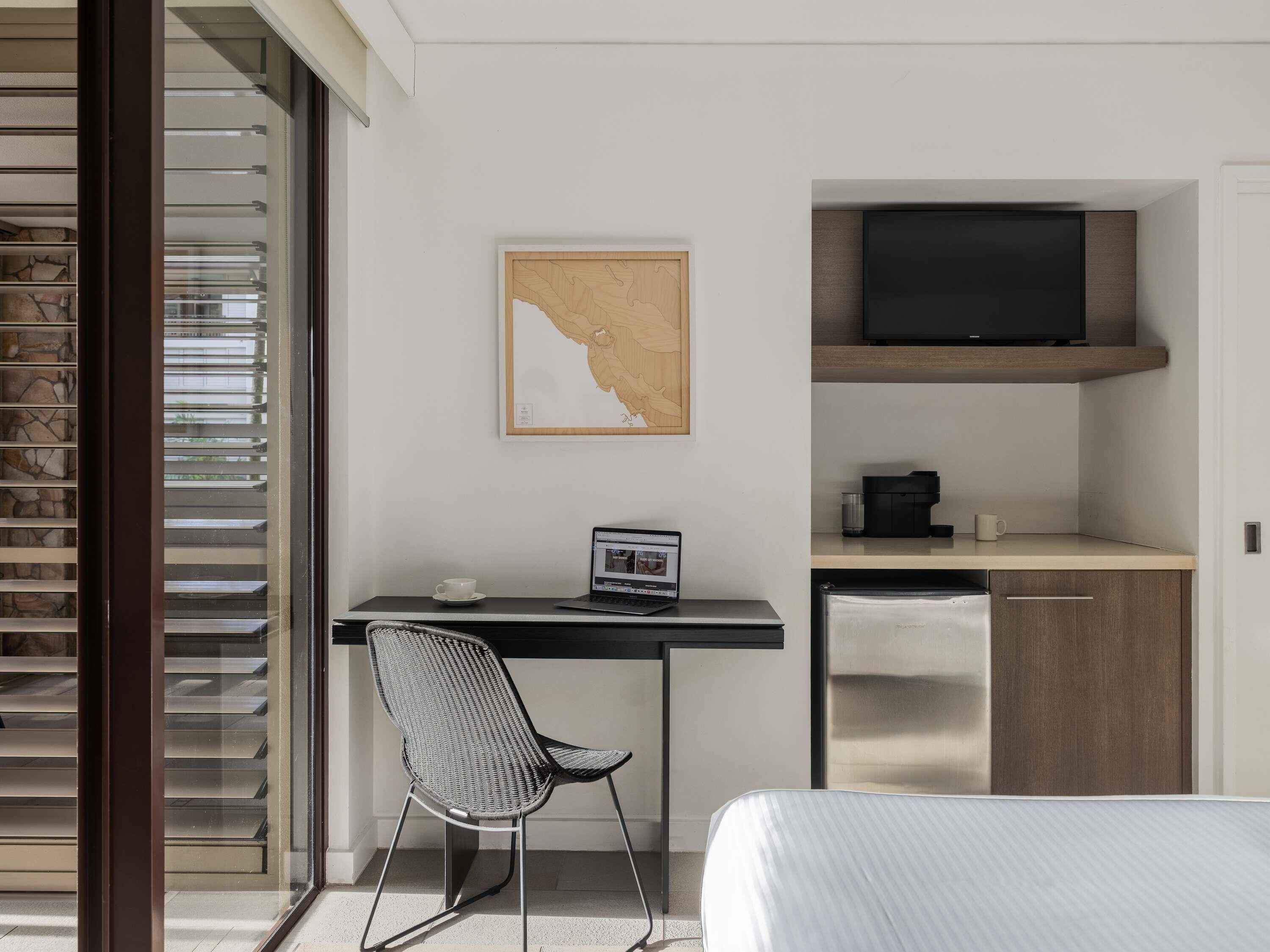 A modern hotel room with a desk, chair, bed, and a television.