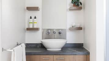 A bathroom with a white sink, wooden cabinets, and two shelves with toiletries.