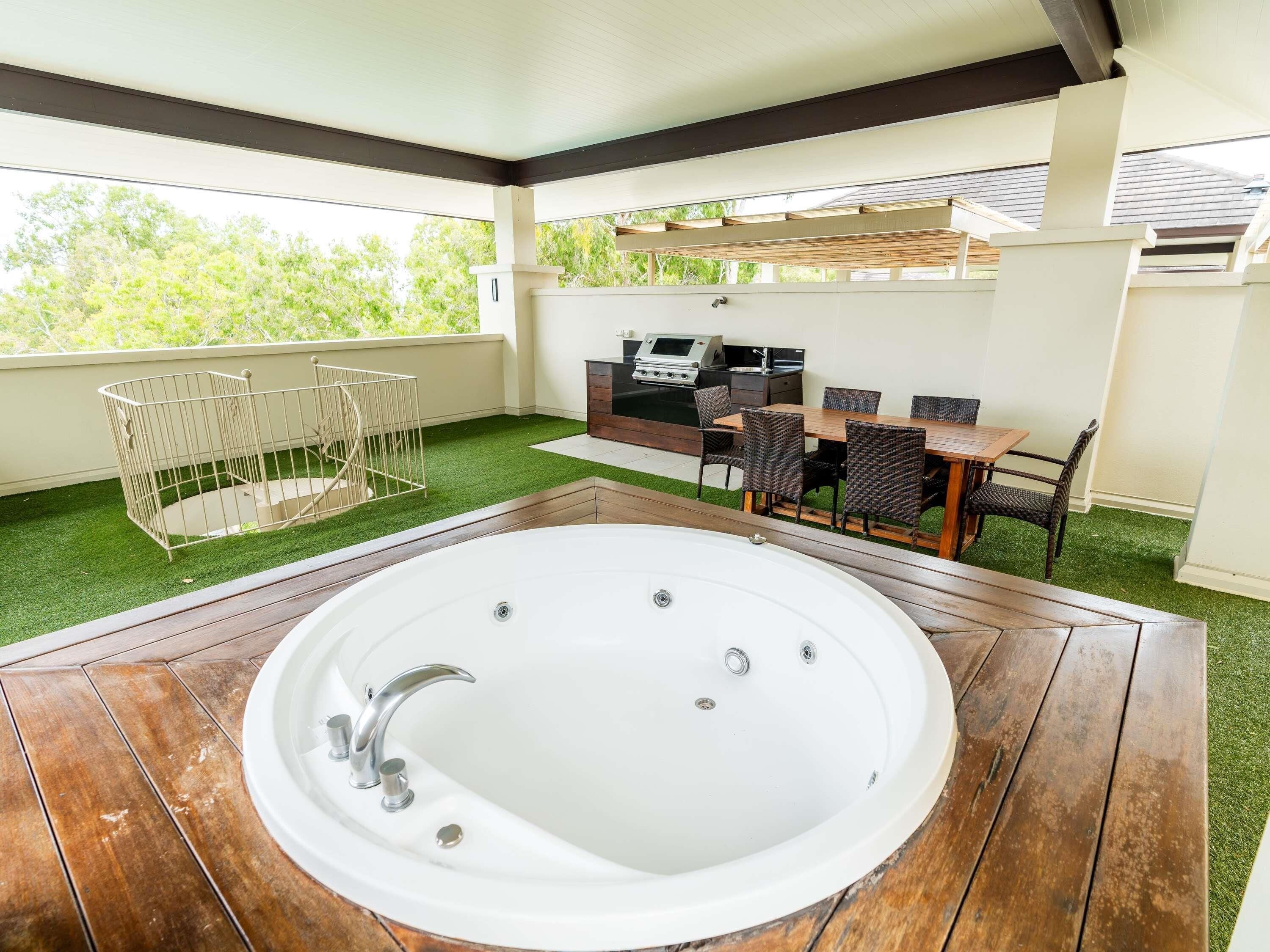 Un patio con jacuzzi, mobiliario exterior y una parrilla.