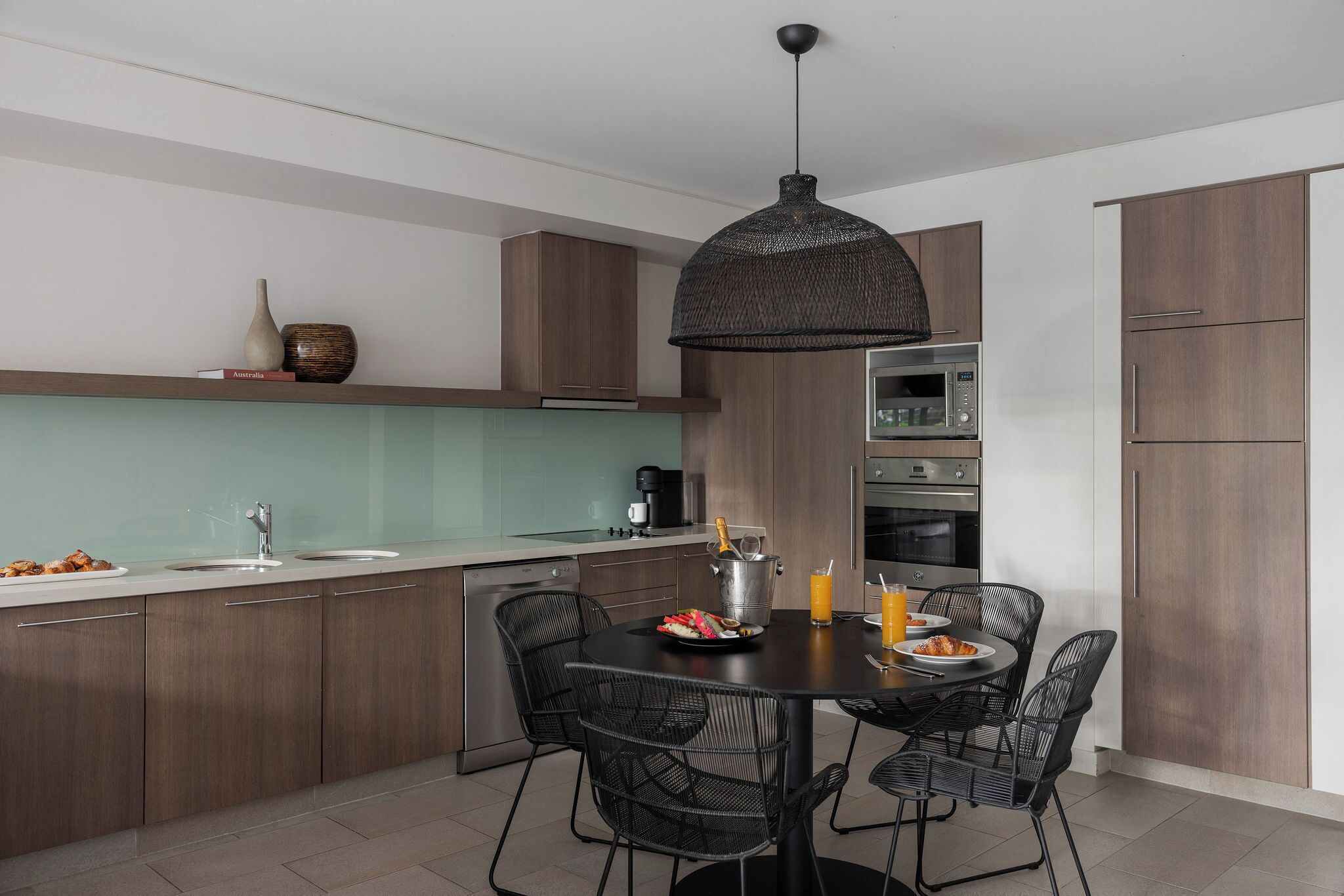 A modern kitchen with a dining area, featuring a central island, dark wooden cabinets, and a hanging light fixture.