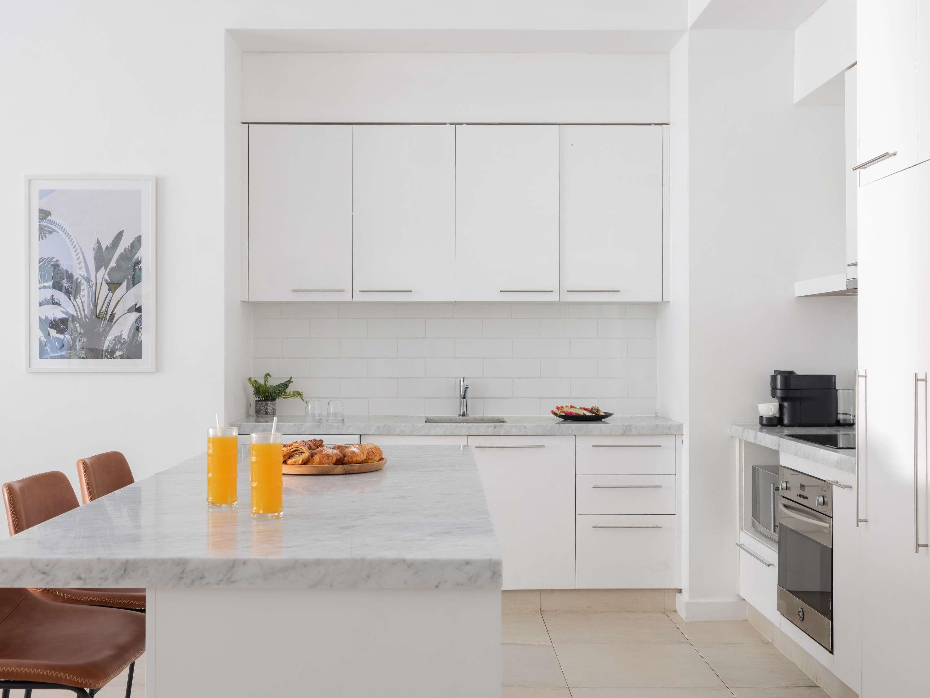 Una cocina moderna con gabinetes blancos, encimera de mármol y comedor con sillas.