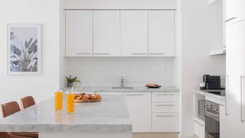 Una cocina moderna con gabinetes blancos, encimera de mármol y comedor con sillas.