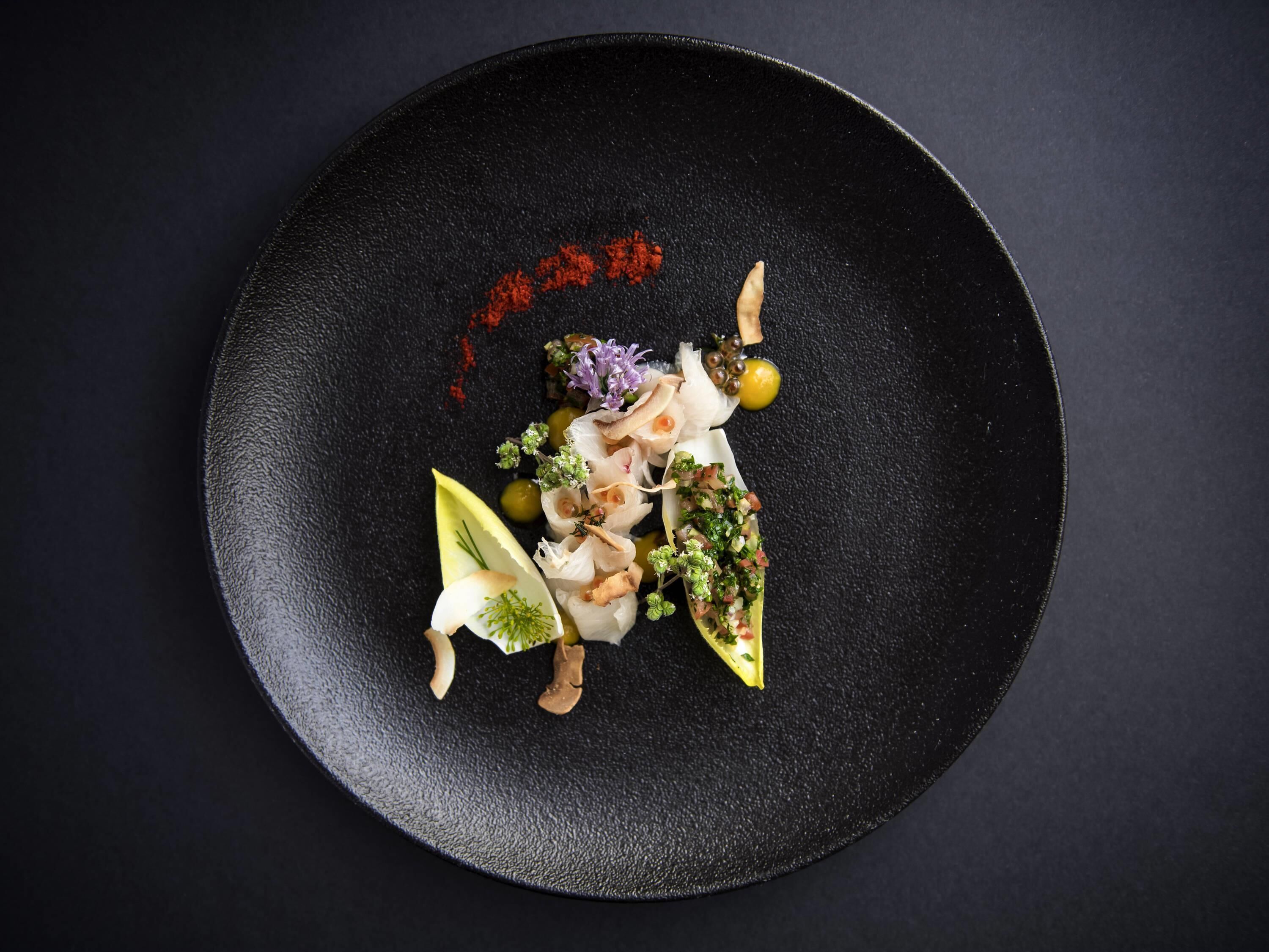 A black plate with a variety of food items and garnishes.