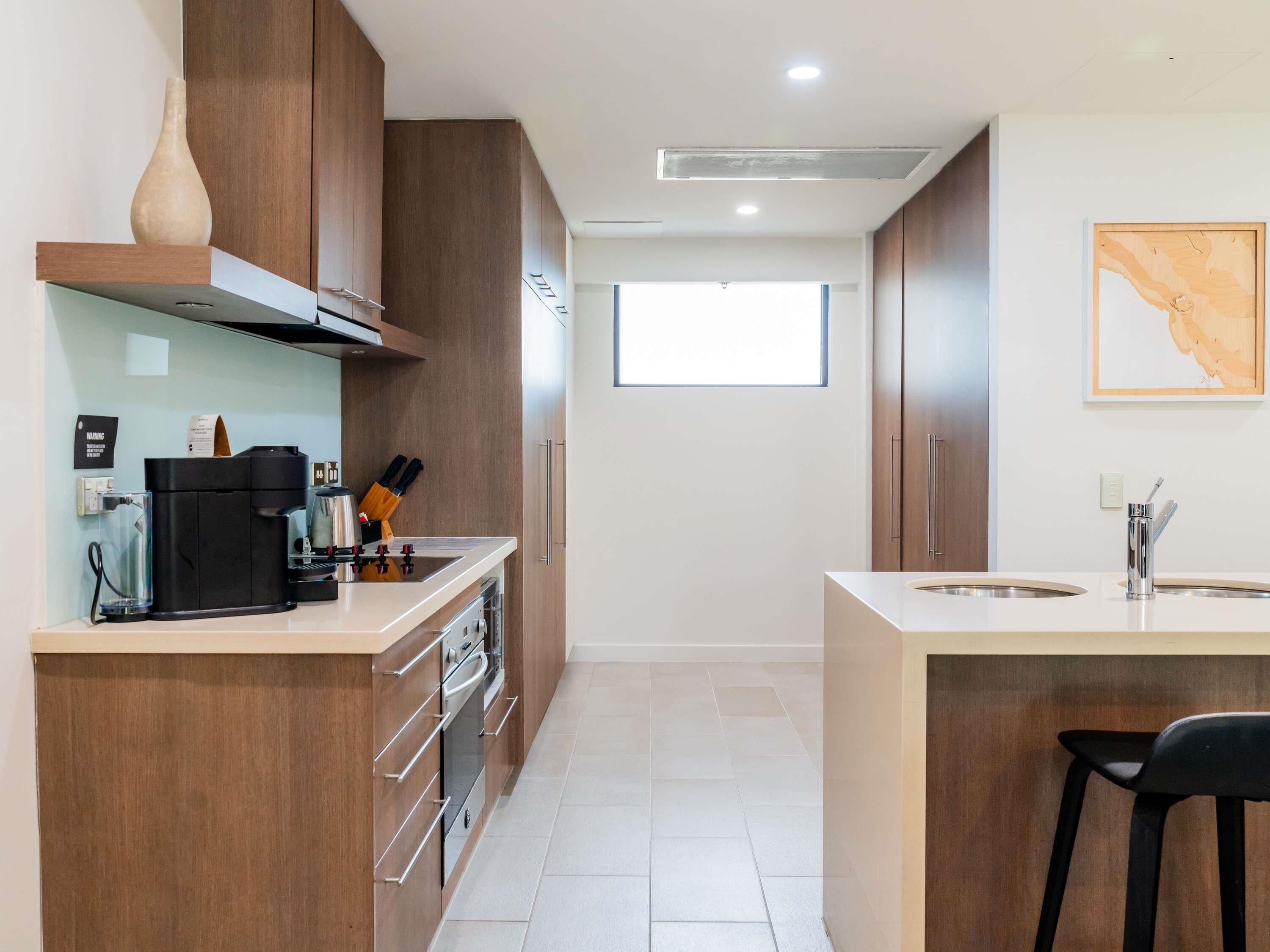 A modern kitchen with wooden cabinets, a coffee machine, and a large window.