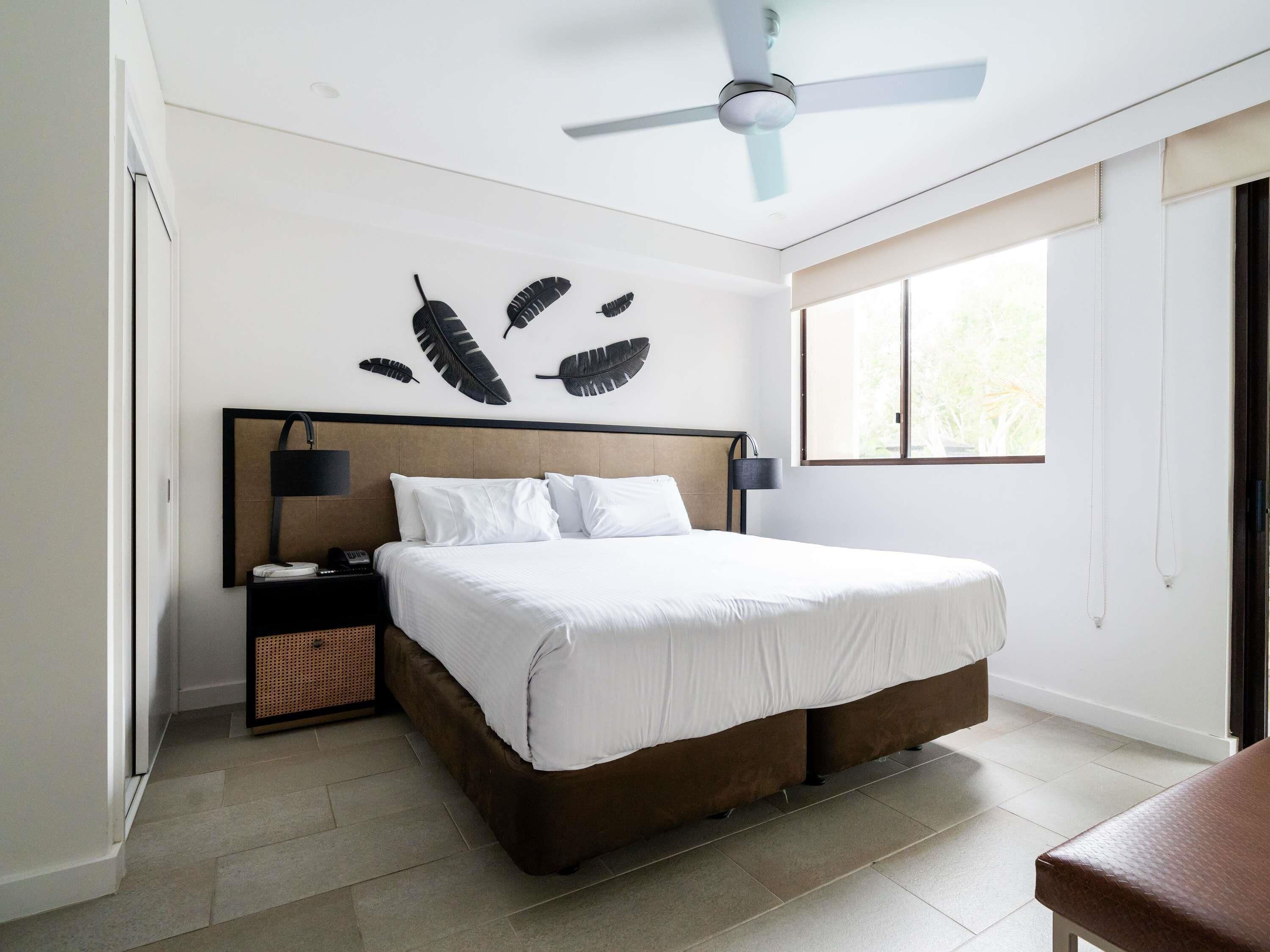 A bedroom with a bed, a ceiling fan, a nightstand, a lamp, and a window.