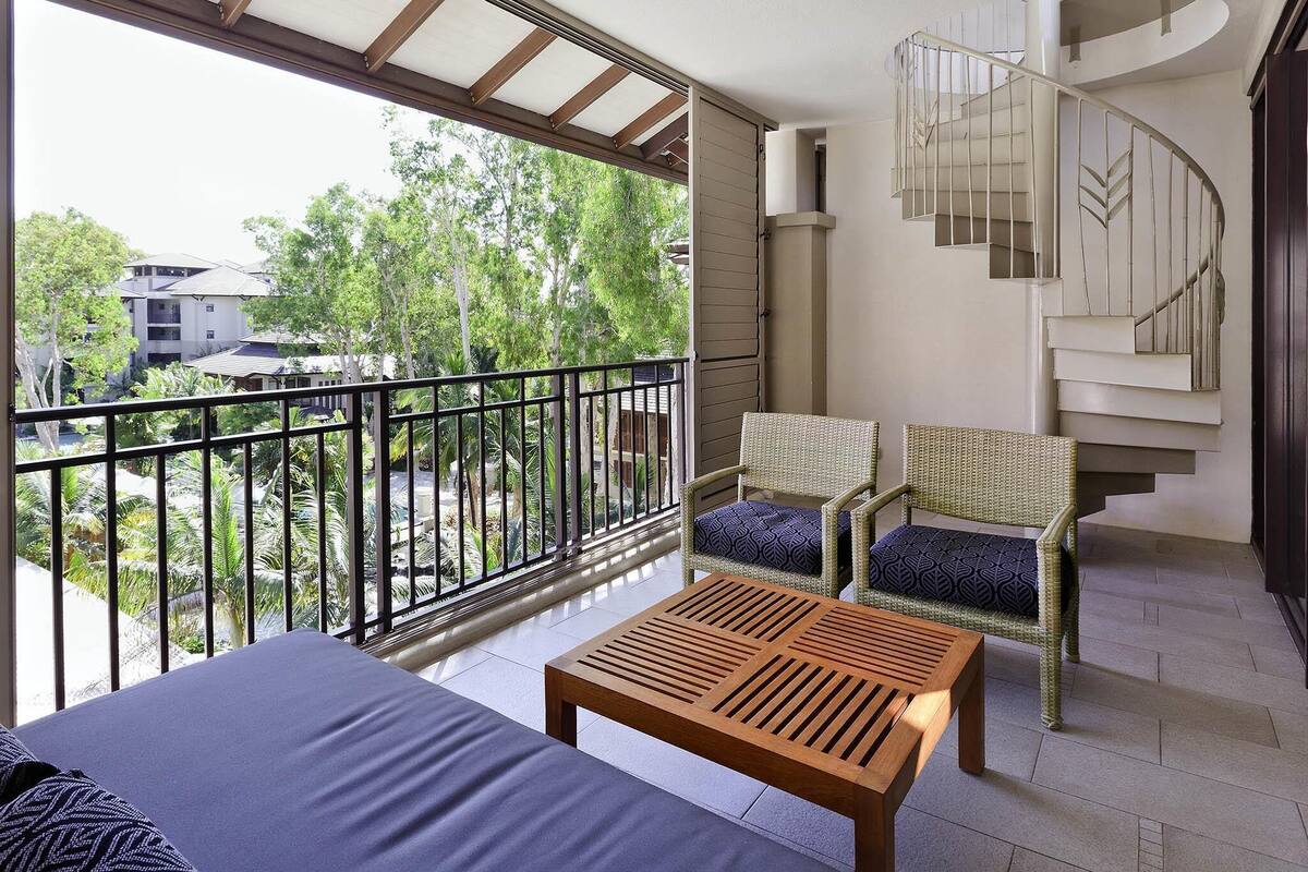 Ein Balkon mit einem Holztisch, Korbstühlen und einer Wendeltreppe.