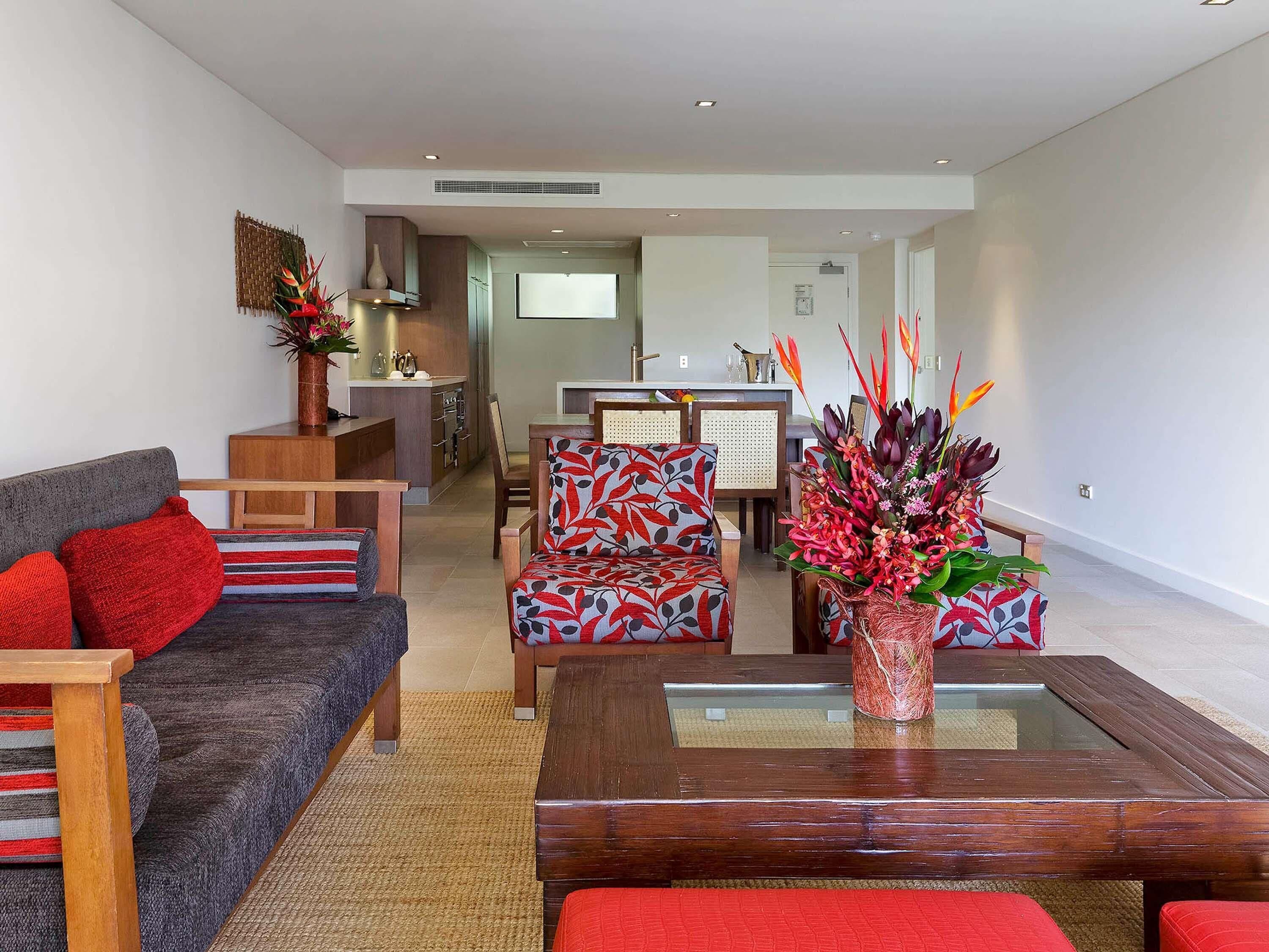 A modern living room with a sofa, chairs, a coffee table, and a kitchen area in the background.