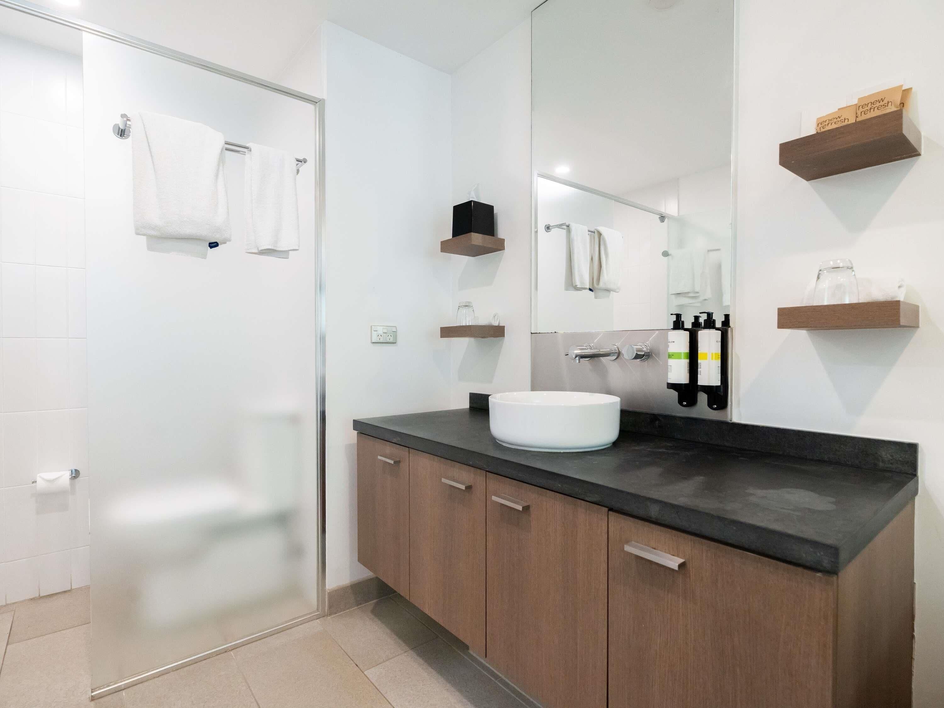 A modern bathroom with a glass shower enclosure, a white sink, wooden cabinets, and a mirror.