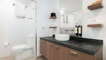 Un baño moderno con cabina de ducha de vidrio, un lavabo blanco, armarios de madera y un espejo.