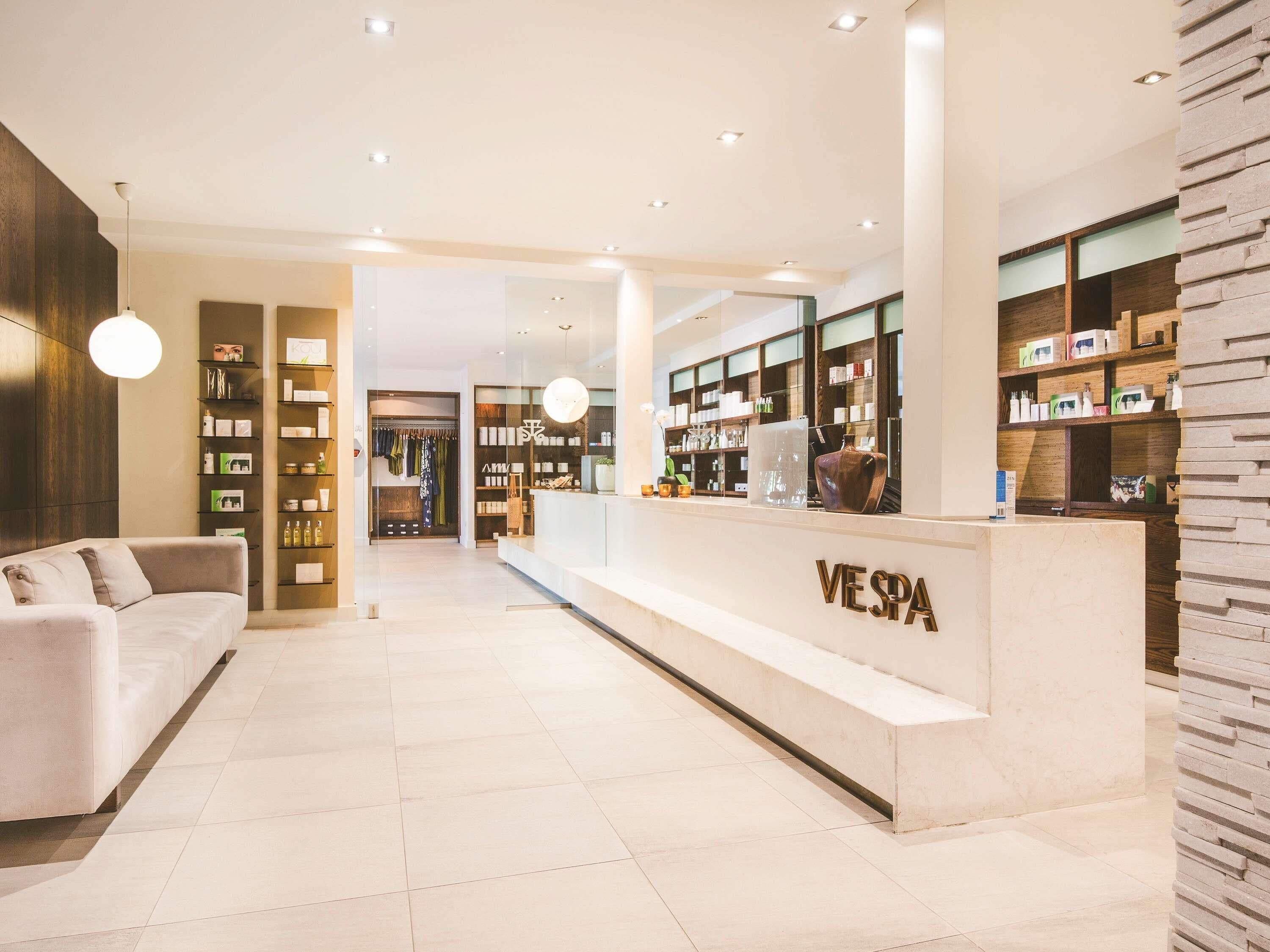 Um interior moderno com uma receção identificada como 'VESPA', uma área de estar e uma loja de roupa.