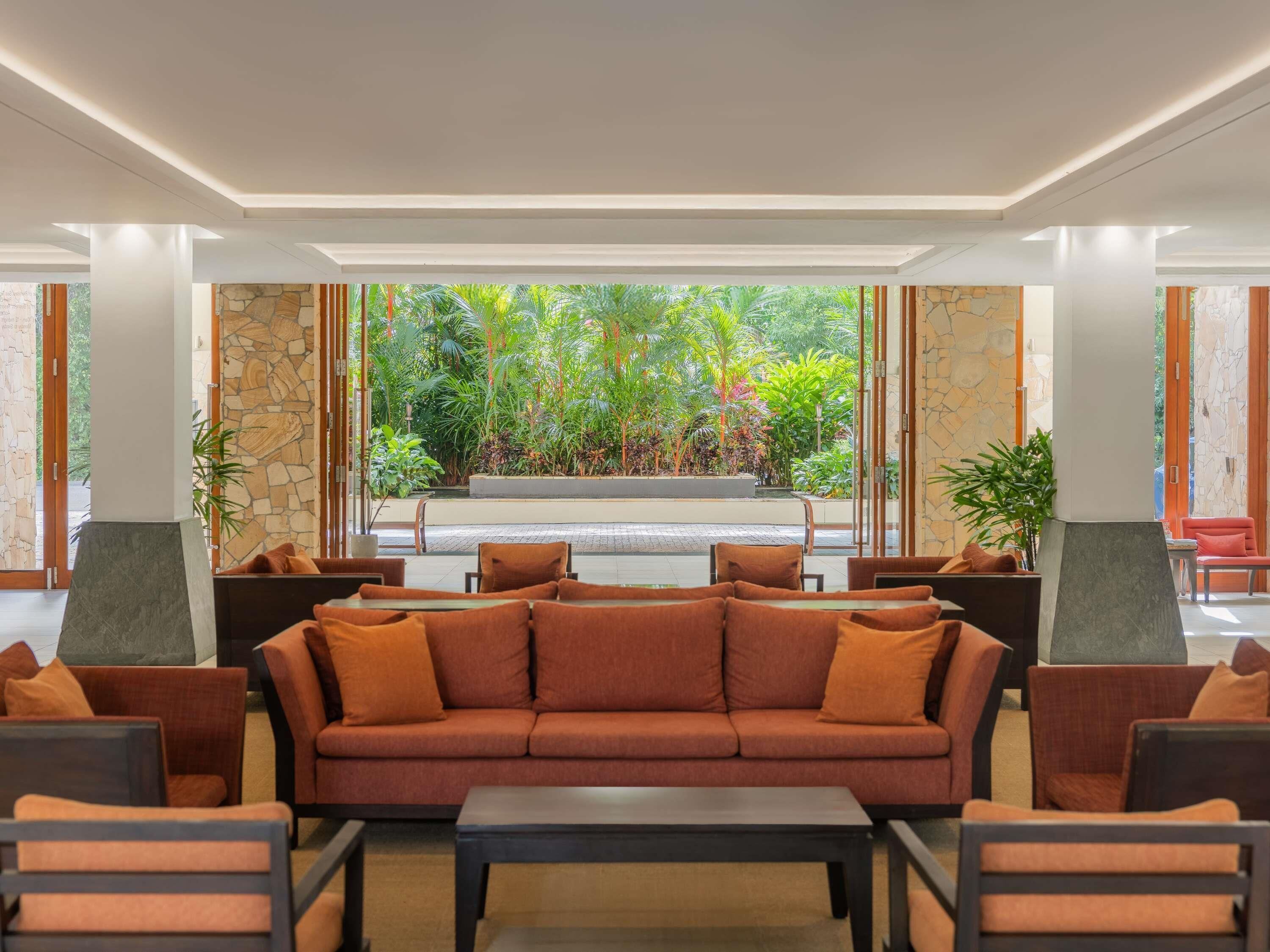 A modern lobby with a sofa, chairs, a coffee table, and a view of a garden through large windows.