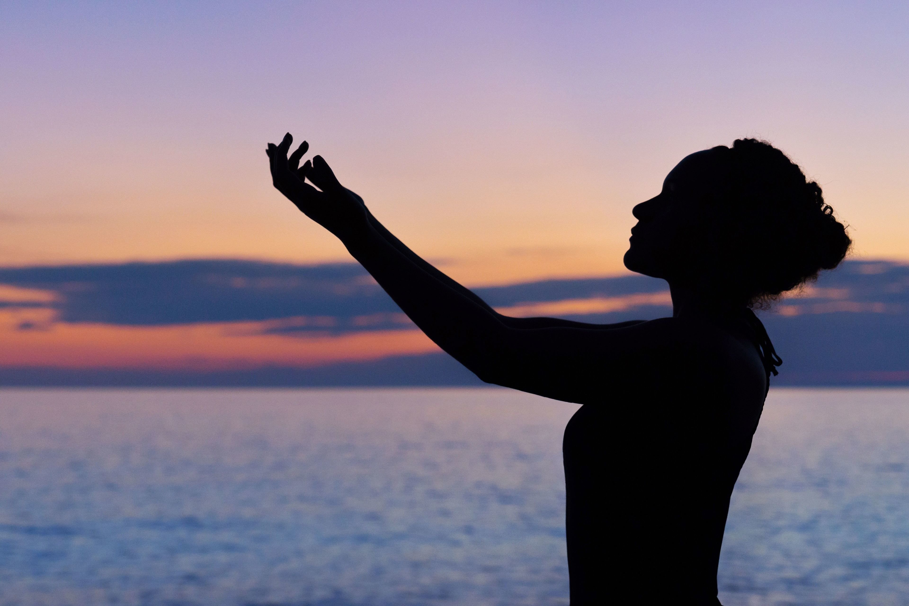 A silhouette of a person with arms raised against a sunset over water.