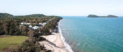 Un paisaje costero con playa, muelle y una pequeña isla en la distancia.