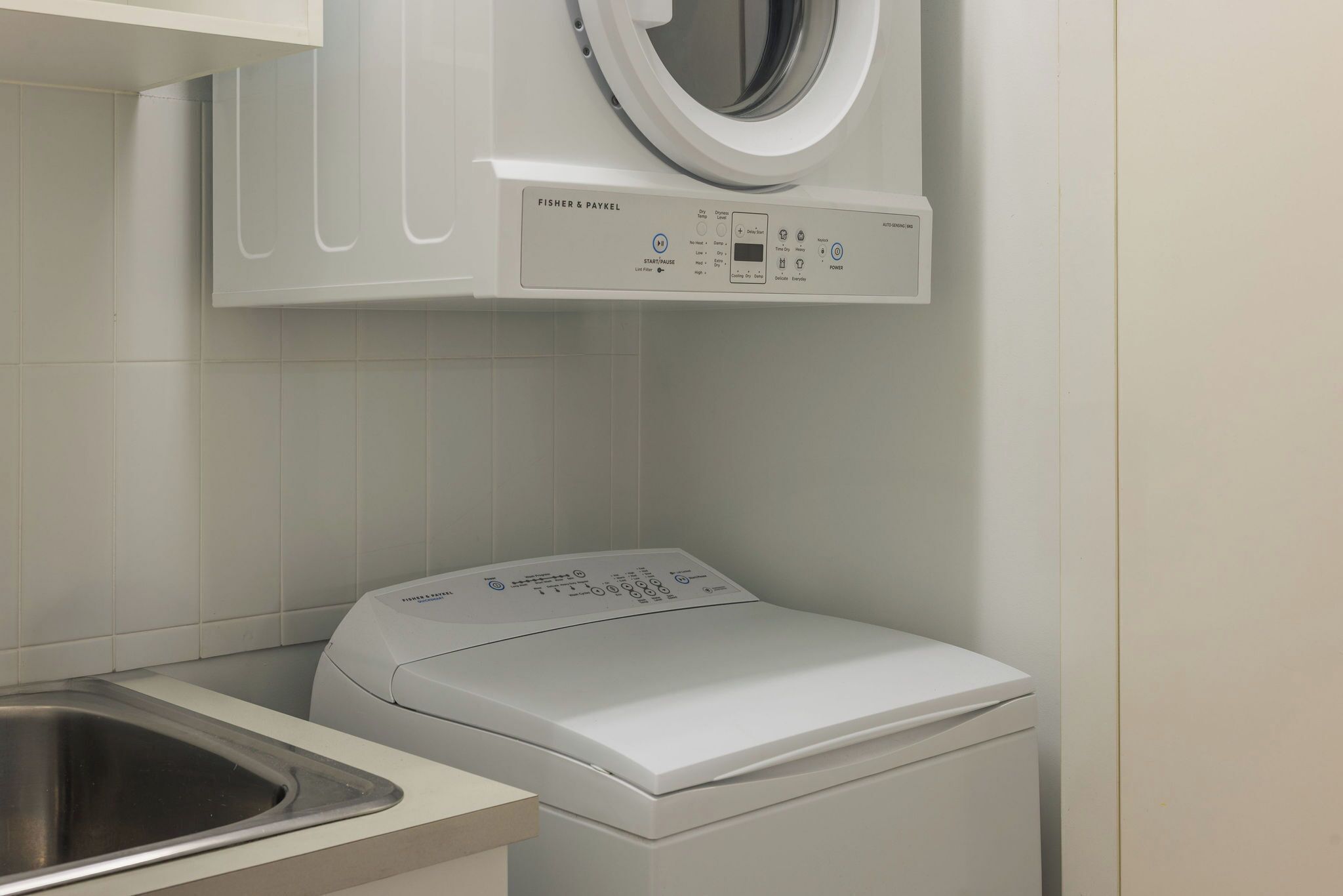 A compact, modern laundry room with a front-loading washer and dryer, a stainless steel sink, and a wall-mounted washing machine.