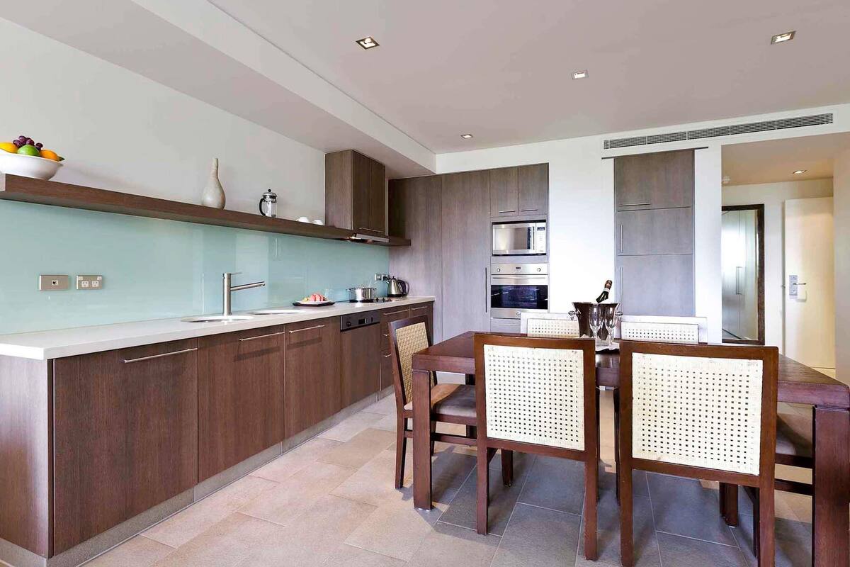 Een moderne keuken met donkerhouten kastjes, een lichtblauwe achterwand en een eethoek met een houten tafel en stoelen.