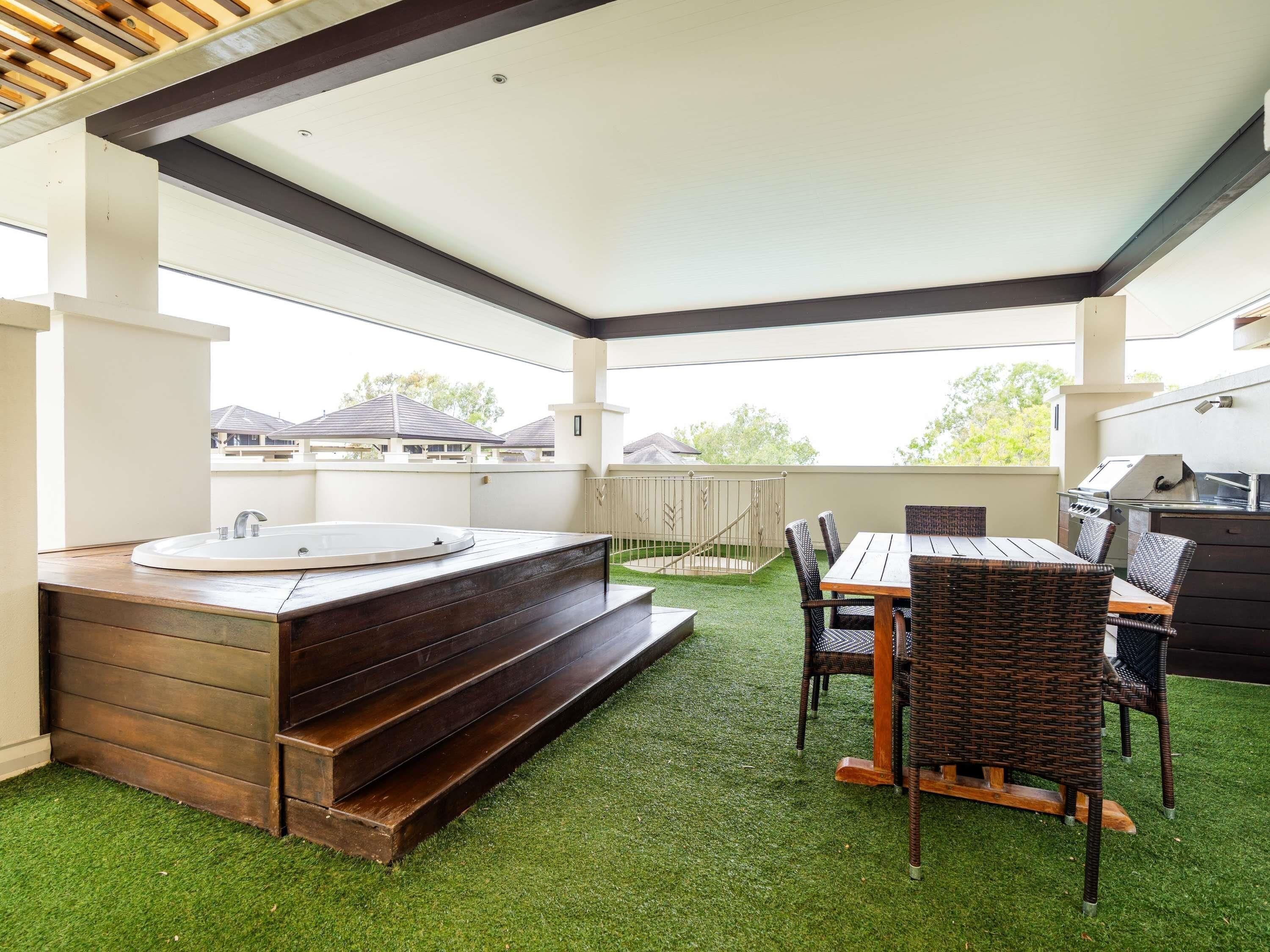 A covered patio with a hot tub, outdoor seating, and a grill.