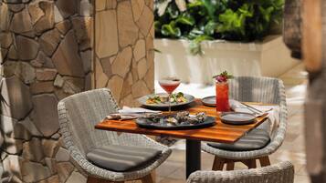 Una mesa de comedor con sillas de mimbre, una pared de piedra y una planta tropical al fondo.