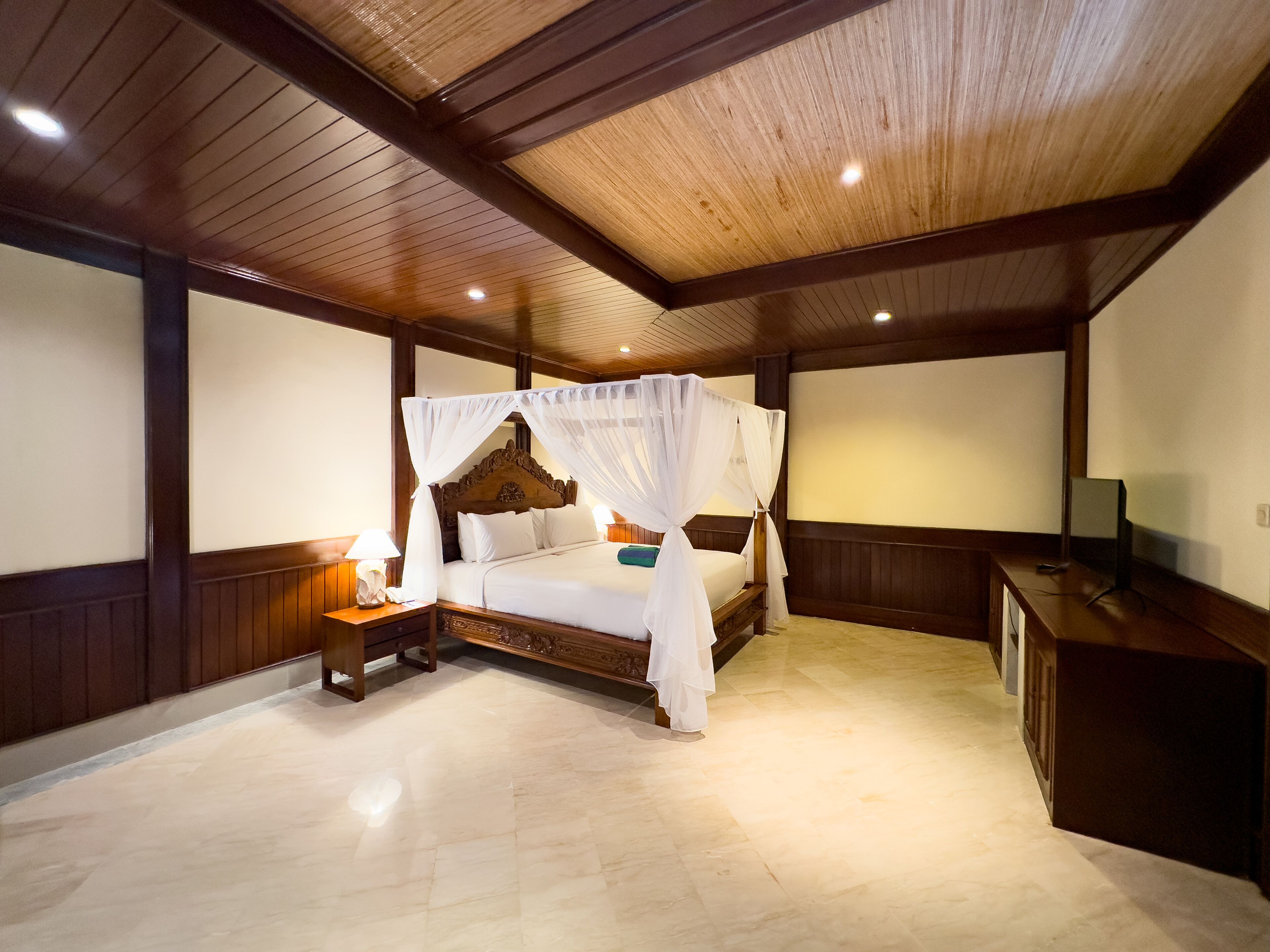 Um quarto espaçoso com uma cama grande, teto de madeira e mesa de cabeceira com abajur.