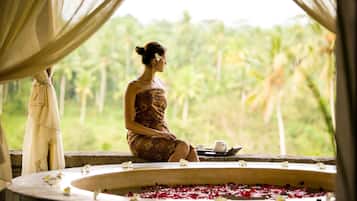 Relax in a serene spa setting with a view of lush greenery, featuring a bathtub, teapot, and refreshments.