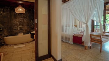 A bedroom with a four-poster bed, a bathtub, and a wooden chair.