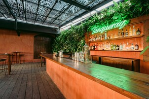 Una zona de bar con mostrador de madera, estanterías llenas de botellas de licores y un letrero de neón.