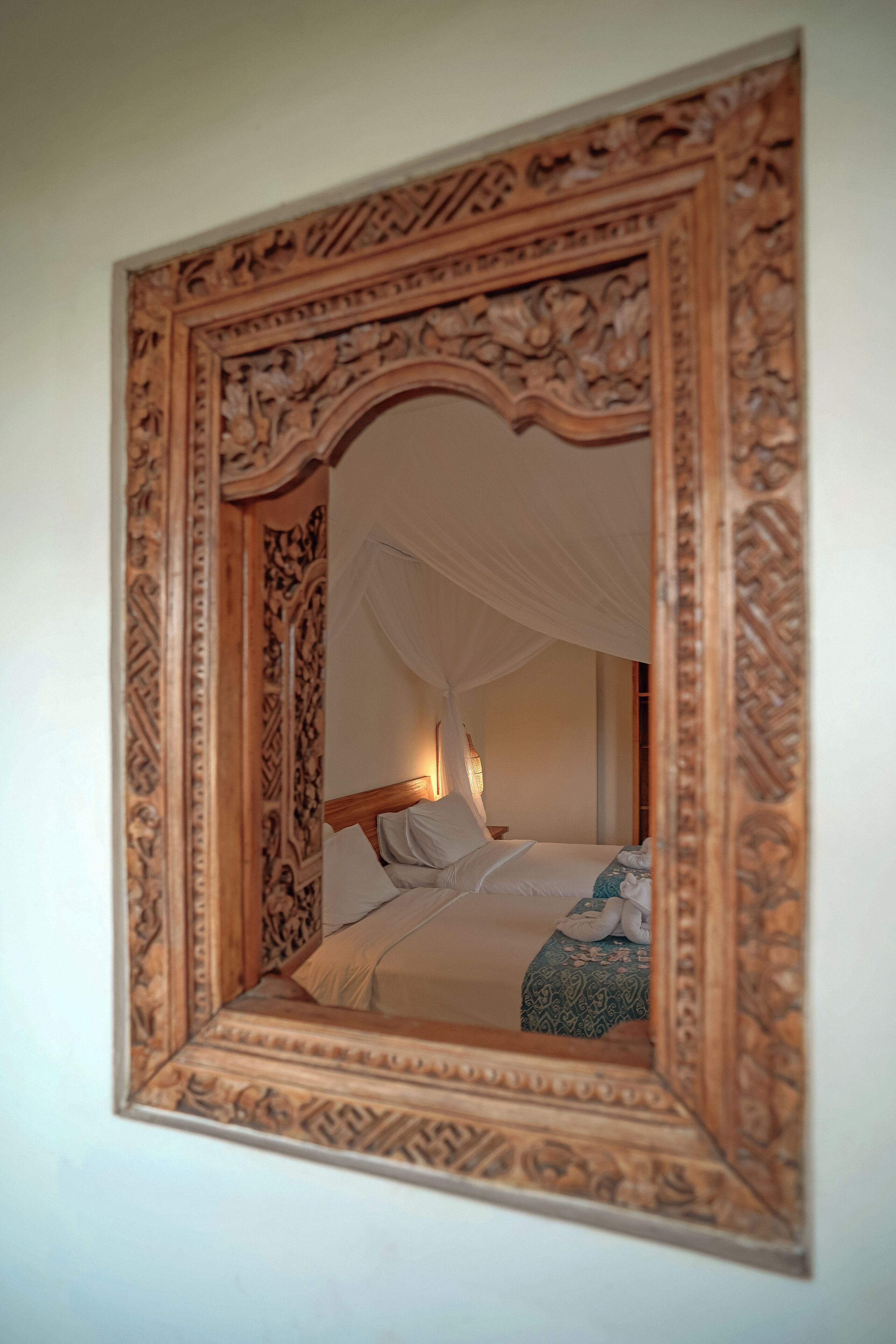 Un espejo con un marco de madera decorativo refleja una cama con dosel.