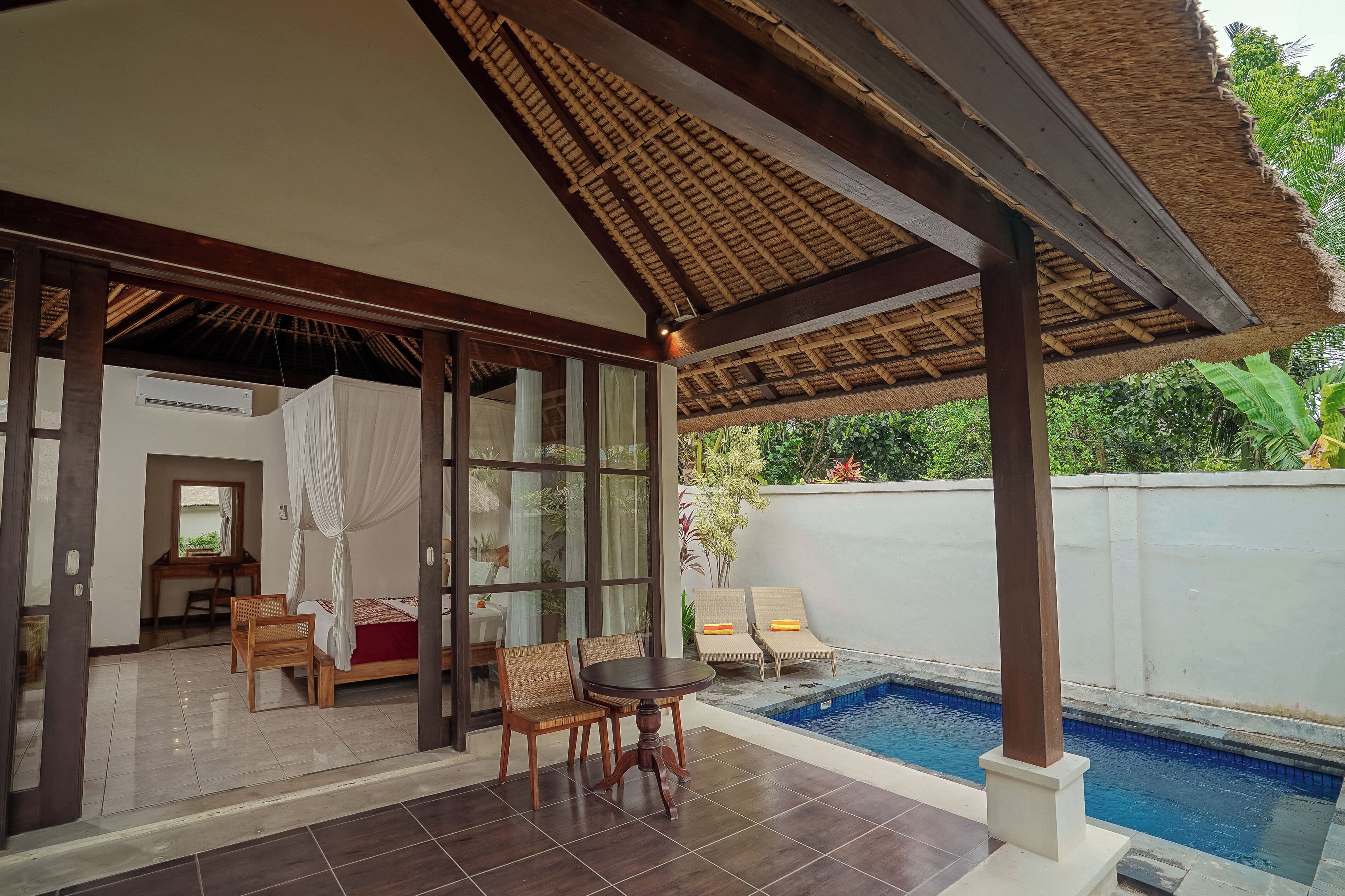 Una habitación con una puerta de cristal que da a un balcón con piscina, una cama con dosel y un escritorio con silla.