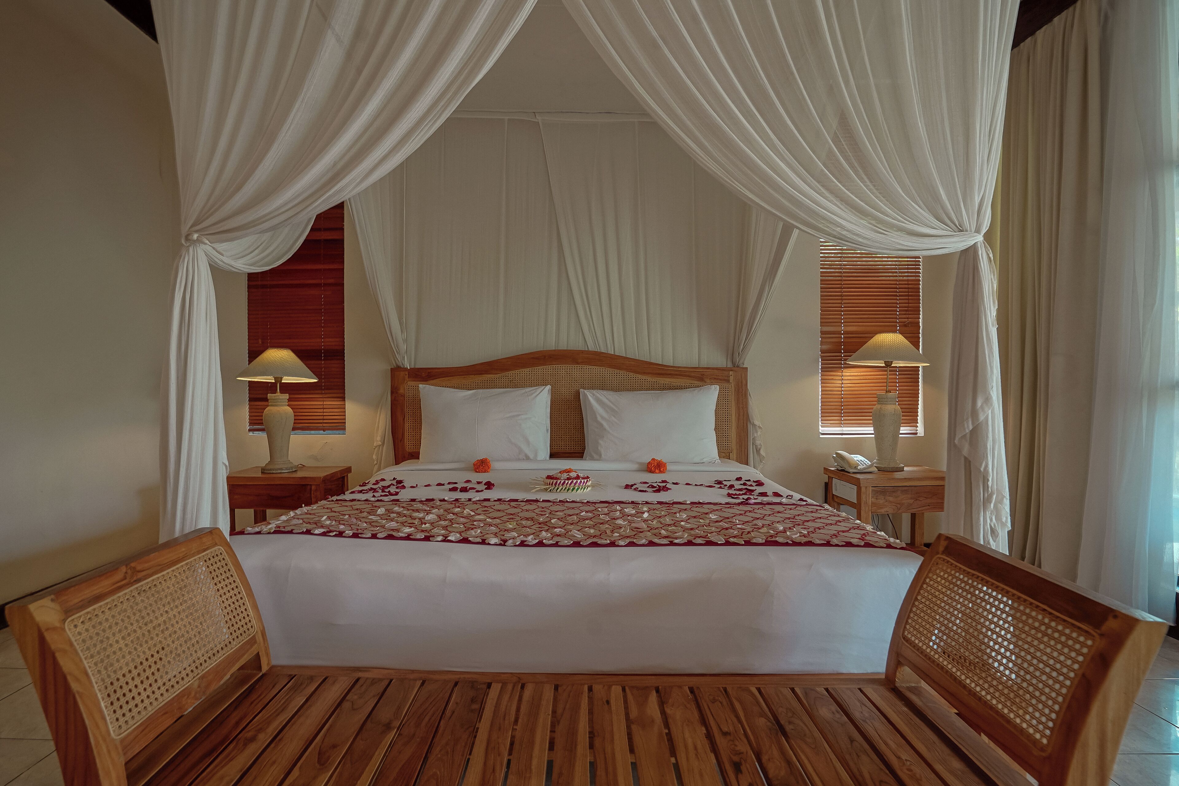 A bed with white linens, a wooden headboard, and a canopy. There are two bedside tables with lamps.