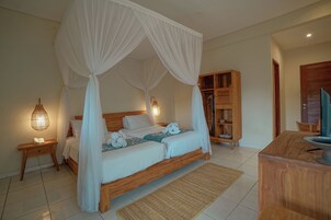 A bedroom with a four-poster canopy bed, bedside lamps, a wooden nightstand, a wooden wardrobe, and a wooden desk with a chair.