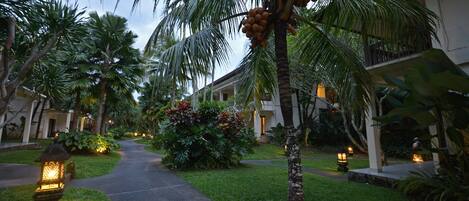 Un camino bordeado de palmeras y un edificio con balcones, evocando un ambiente de resort.