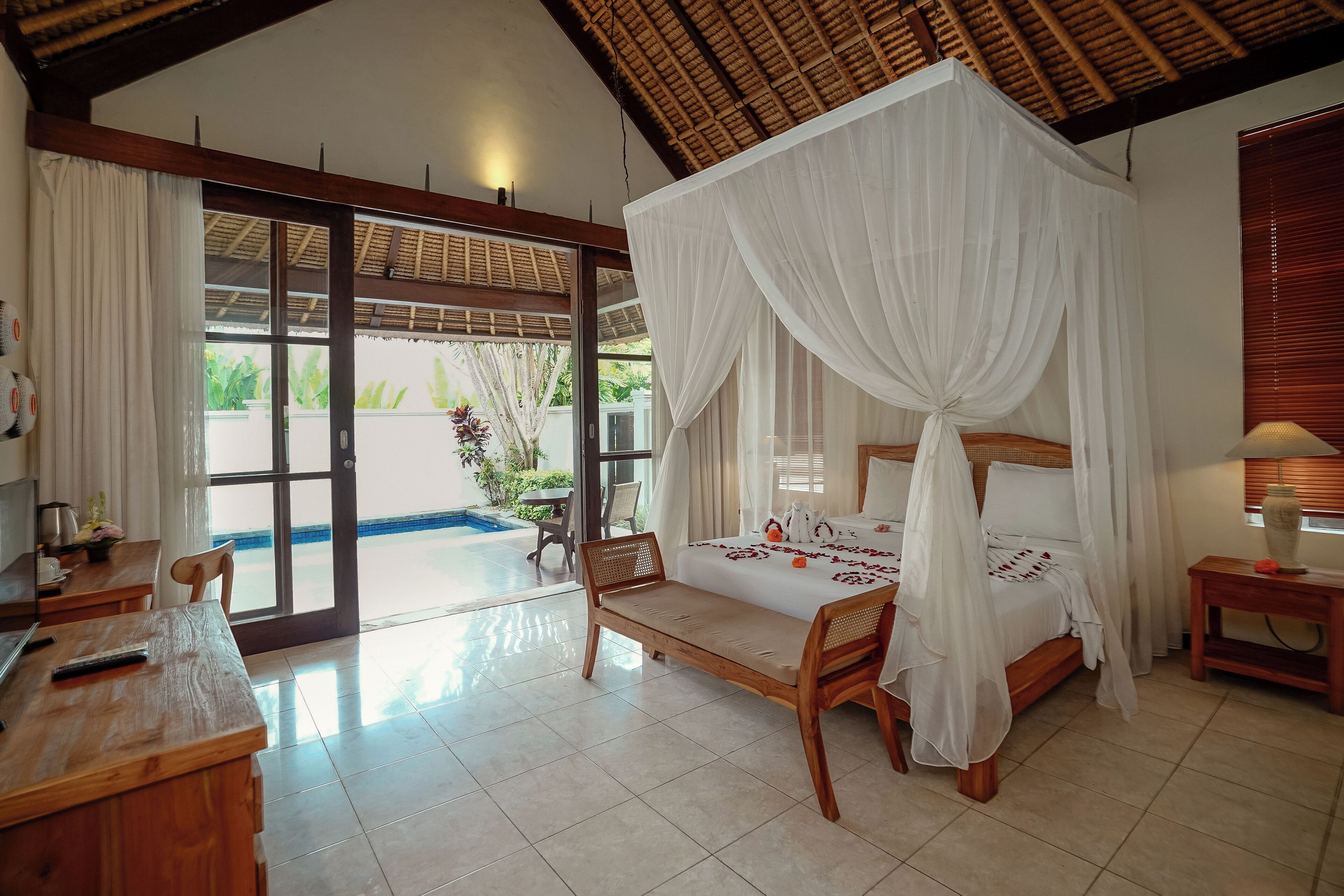 A bedroom with a four-poster bed, wooden furniture, and a view of a swimming pool.