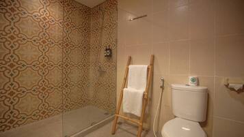 A bathroom with patterned tiles, a glass shower enclosure, a wooden towel rack, and a toilet with a paper towel dispenser.